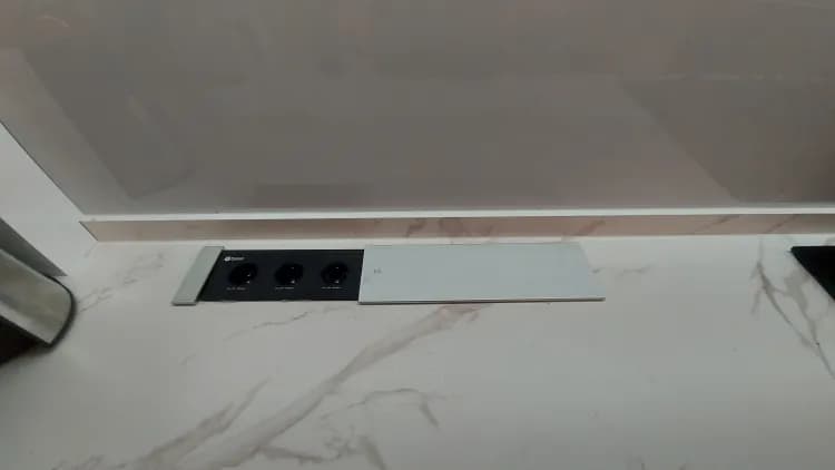 نمای نزدیک از پریز توکار کشویی روی صفحه کابینت طرح سنگ، شامل سه سوکت برق و یک درپوش فلزی