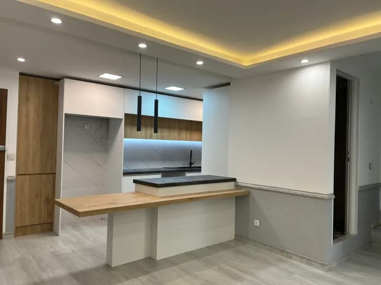 آشپزخانه مدرن اپن با کابینت سفید و طرح چوب به همراه کانتر و نورپردازی مخفی